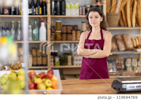 Confident salesgirl standing with arms crossed at counter in grocery store 119694769