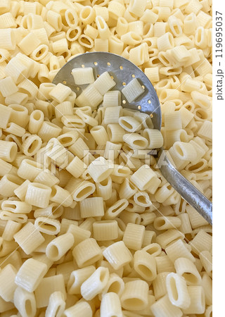 Close-Up of Cooked Turkish Ditalini Pasta with Perforated Serving Spoon in Kitchen Setting.A detailed, close-up shot of cooked ditalini pasta, commonly used in Turkish cuisine 119695037