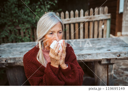 Senior women feeling sick, blowing her runny, stuffy nose into tissue and sneezing. Senior women feeling sick, blowing her runny, stuffy nose into tissue and sneezing. 119695149