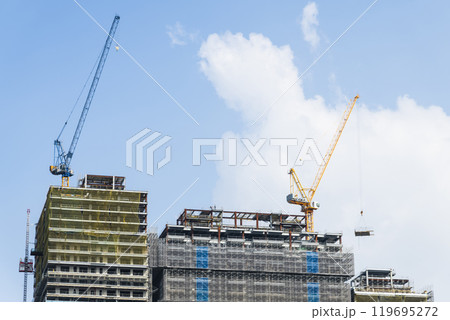 Low-angle view of cranes and steel structures of building construction with a blue sky background. Low-angle view of cranes and steel structures of building construction with a blue sky background. 119695272