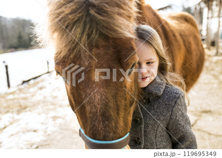 Young girl spending cold winter weekend on family farm, taking care of her brown fluffy pony, hugging him. Young girl spending cold winter weekend on family farm, taking care of her brown fluffy pony, hugging him. 119695349