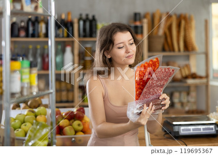 Girl pondering over choice of cured sausages in grocery shop Girl pondering over choice of cured sausages in grocery shop 119695367
