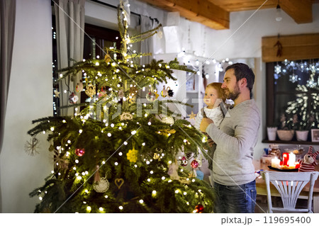 Father showing christmas tree to little son in Christmas home. Cute baby boy is amazed by christmas decorations. 119695400