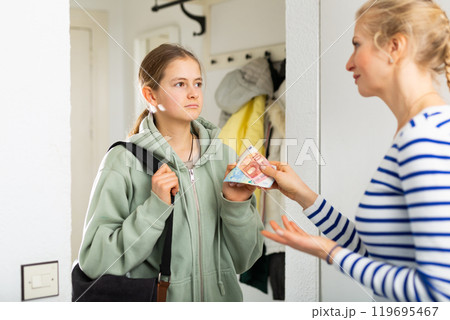 Mom gives pocket money to daughter in the hallway of apartment 119695467