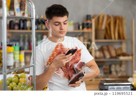 Positive guy purchaser scanning with smartphone QR code of dried sausage or meat in supermarket 119695521