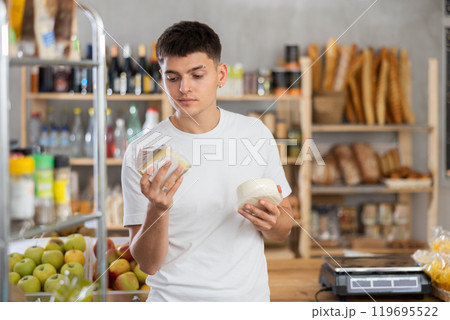 Guy carefully chooses tasty cheese in grocery store Guy carefully chooses tasty cheese in grocery store 119695522