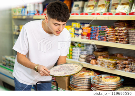 in supermarket in department of semi-finished products, man chooses pizza in supermarket in department of semi-finished products, man chooses pizza 119695550