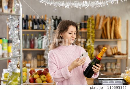 Young girl is scanning QR on spark wine bottle in grocery store during New Year Young girl is scanning QR on spark wine bottle in grocery store during New Year 119695555