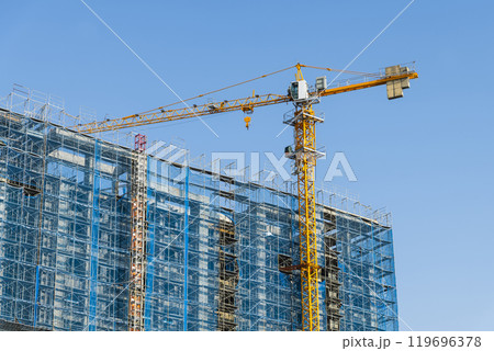 Low-angle view of cranes and steel structures of building construction with a blue sky background. 119696378