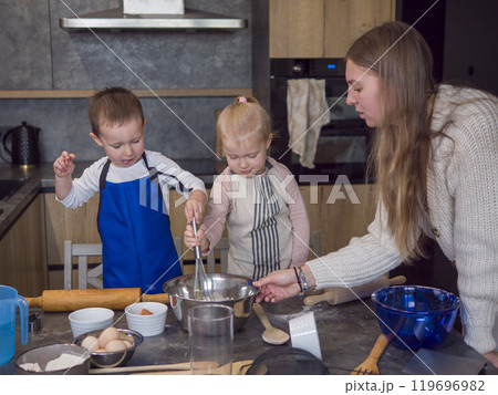 Mother guides her kids in a modern kitchen, making cookie dough together. They bond over baking, learning skills, and creating memories, concept of cooking food from dough, cook at home Mother guides her kids in a modern kitchen, making cookie dough together. They bond over baking, learning skills, and creating memories, concept of cooking food from dough, cook at home 119696982