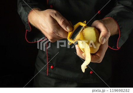Chef peels raw potatoes with a vegetable peeler. Preparing to cook potato dish or mashed potatoes by the hands of the cook 119698282