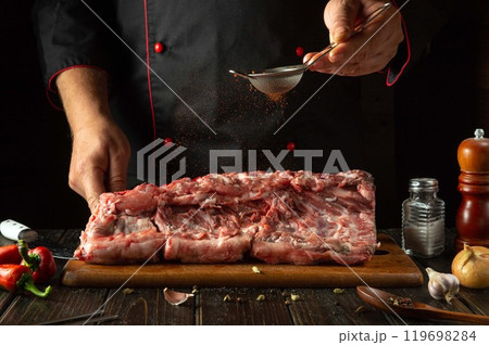 Adding paprika to raw meat manually by a chef for aroma and taste. The process of cooking pork ribs on the kitchen table with spices and aromatic pepper Adding paprika to raw meat manually by a chef for aroma and taste. The process of cooking pork ribs on the kitchen table with spices and aromatic pepper 119698284