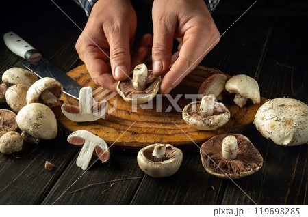 Chef sorts champignons mushrooms on the kitchen table before cooking. Concept of preparing mushrooms for a delicious dinner or breakfast Chef sorts champignons mushrooms on the kitchen table before cooking. Concept of preparing mushrooms for a delicious dinner or breakfast 119698285
