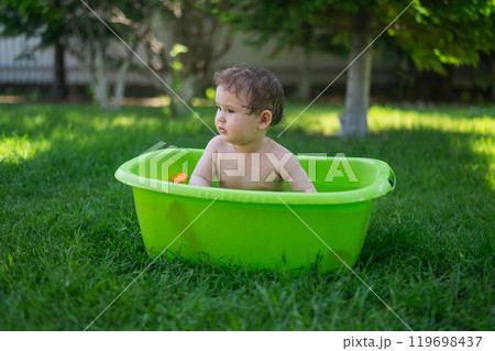 Cute baby boy bathes in a basin outdoors in summer. Cute baby boy bathes in a basin outdoors in summer. 119698437