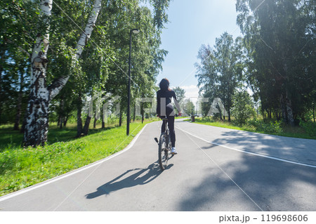Rear view of Caucasian woman riding bike in park. Rear view of Caucasian woman riding bike in park. 119698606