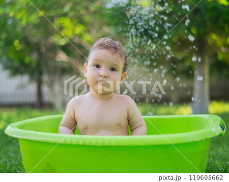 Cute baby boy bathes in a basin outdoors in summer. 119698662