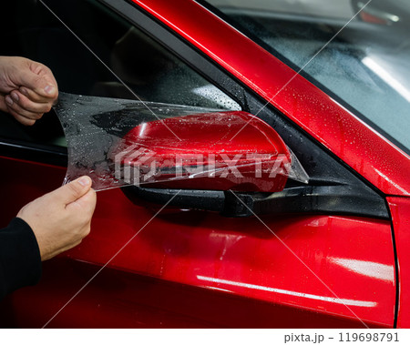 The master applies vinyl film to the side view mirror of a car.  119698791