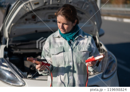 Woman holding clamps for charging a car battery. Woman holding clamps for charging a car battery. 119698824