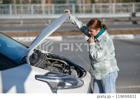 Caucasian woman looks puzzled under the hood of a car. Caucasian woman looks puzzled under the hood of a car. 119698831