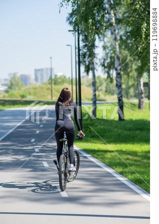 Rear view of Caucasian woman riding bike in park. Vertical photo. Rear view of Caucasian woman riding bike in park. Vertical photo. 119698884