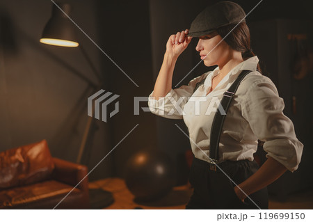 Caucasian woman in a Peaky Blinders style men's suit posing in a retro gym. 119699150