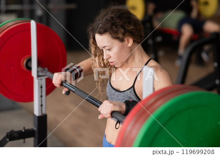 Middle-aged woman doing squats with a barbell in the gym.  119699208