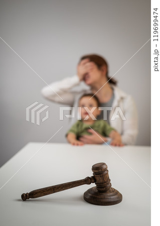 Caucasian woman crying with baby in her arms behind judge's gavel divorce.  119699474