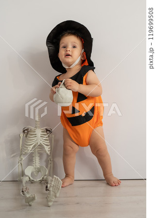 Cute caucasian boy in pumpkin costume for halloween holding skull on white background.  119699508