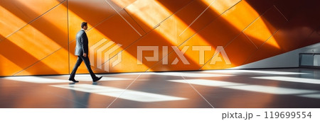 Confident businessman walking in contemporary airport terminal, bathed in warm sunlight. Modern architecture creates spacious, bright atmosphere with geometric lines and shadows 119699554