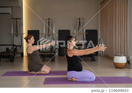 Two pregnant women doing yoga. Exercises with a gymnastic circle for Pilates.  119699683