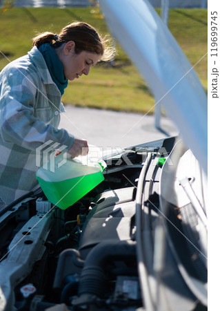 Caucasian woman filling car reservoir with windshield washer fluid from bottle.  119699745
