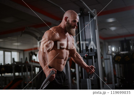 Bald Caucasian bodybuilder training chest using cable crossover in gym. Bald Caucasian bodybuilder training chest using cable crossover in gym. 119699835