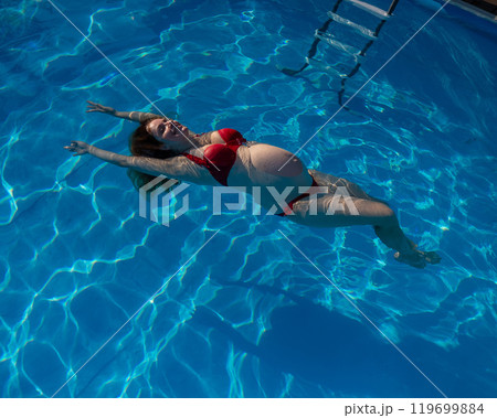 Top view of pregnant woman floating in pool in red bikini.  119699884