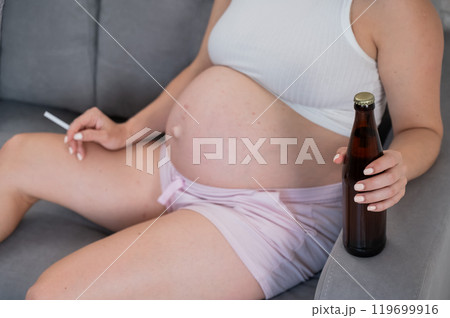 Faceless pregnant woman drinks beer while sitting on the sofa.  119699916
