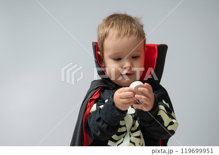 Little Caucasian boy in Dracula costume holding candle on white background.  119699951