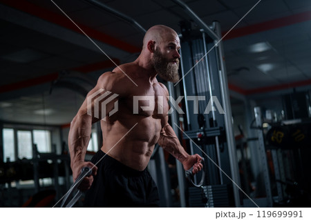 Bald Caucasian bodybuilder training chest using cable crossover in gym.  119699991