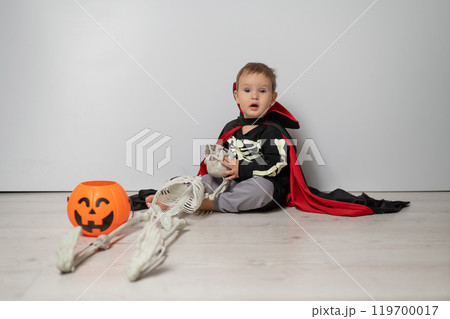 Little Caucasian boy in Dracula costume holding skull on white background. Little Caucasian boy in Dracula costume holding skull on white background. 119700017