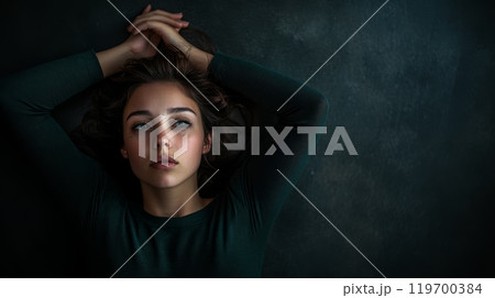 Young woman lies on the floor, showing deep sadness and pain, feeling lonely and stressed, lost in thought about her problems, seeking help for mental health issues 119700384