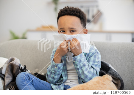 Young boy with cold blowing nose on couch at home 119700569