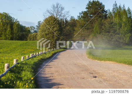 Empty rural road with wooden fence on the roadside and road dust Empty rural road with wooden fence on the roadside and road dust 119700876