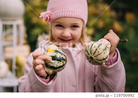 Young girl in a pink hat joyfully holding decorative gourds during autumn 119700992