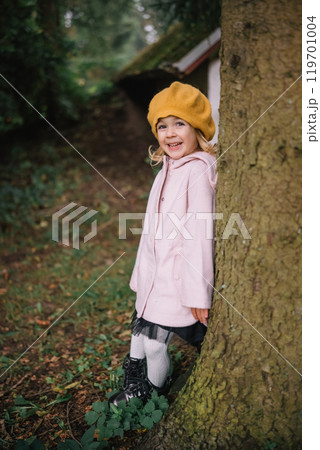 Young child in a yellow beret enjoying nature near a tree during a sunny day in the woods Young child in a yellow beret enjoying nature near a tree during a sunny day in the woods 119701004
