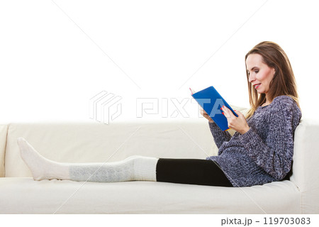 Woman sitting on couch reading book at home 119703083