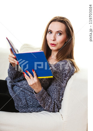 Woman sitting on couch reading book at home Woman sitting on couch reading book at home 119703084
