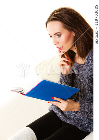 Woman sitting on couch reading book at home Woman sitting on couch reading book at home 119703085