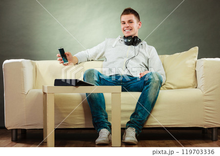 man on couch with headphones smartphone and tablet 119703336