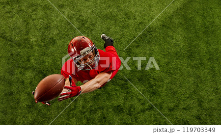 Top view image of concentrated man, American football player in red uniform in motion on stadium, catching ball with precision Top view image of concentrated man, American football player in red uniform in motion on stadium, catching ball with precision 119703349