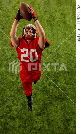 Top view image of concentrated man, American football player in red uniform in motion on stadium, catching ball with precision Top view image of concentrated man, American football player in red uniform in motion on stadium, catching ball with precision 119703358