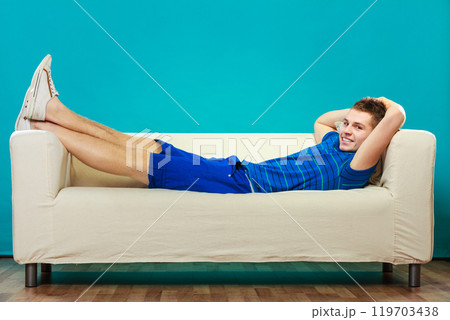 Young man relaxing on couch on blue Young man relaxing on couch on blue 119703438