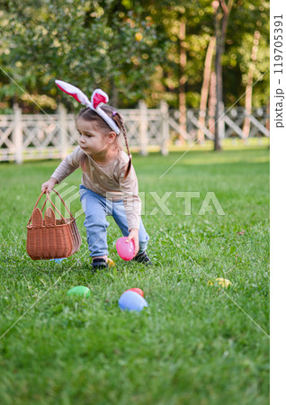 Smiling Little Girl with Bunny Ears and Easter Basket Outdoors 119705391